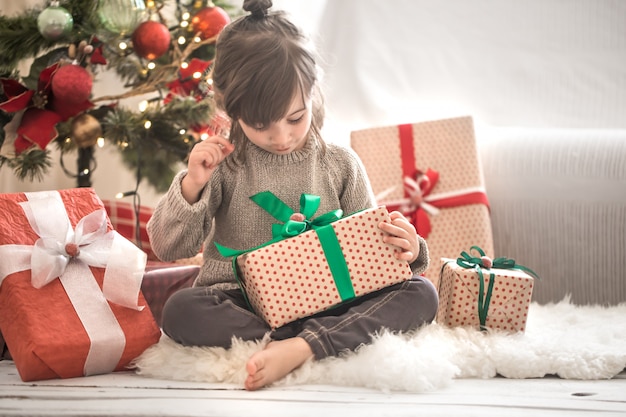 Hübsches kleines Mädchen hält eine Geschenkbox und lächelt, während sie auf ihrem Bett in ihrem Zimmer zu Hause sitzt