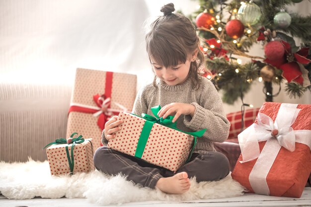 Hübsches kleines Mädchen hält eine Geschenkbox und lächelt, während sie auf ihrem Bett in ihrem Zimmer zu Hause sitzt
