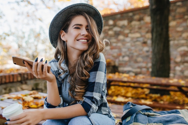 Hübsches lachendes Mädchen mit Smartphone hat eine gute Zeit im Herbstwochenende