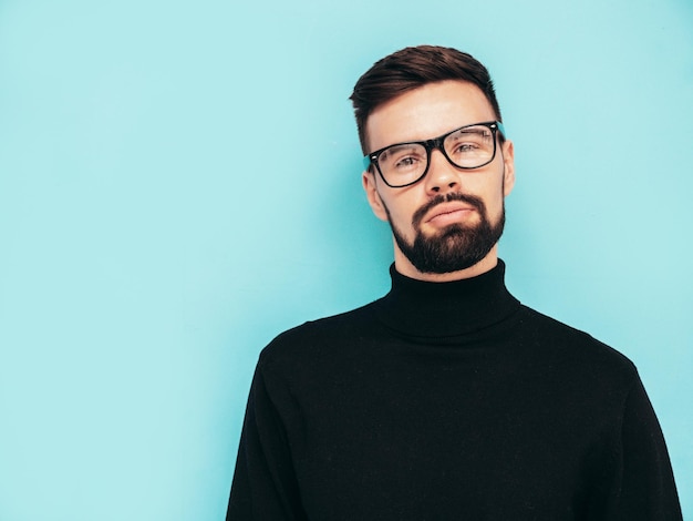 Kostenloses Foto hübsches lächelndes modell sexy stilvoller mann in schwarzem rollkragenpullover und jeans gekleidet mode-hipster-männchen posiert in der nähe der blauen wand im studio isoliert