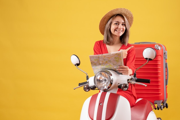 hübsches Mädchen auf Moped, das eine Karte hält, die auf ihren Koffer zeigt