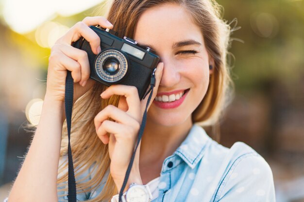 Hübsches Mädchen, das Fotos mit einer Weinlesekamera an einem sonnigen Tag macht