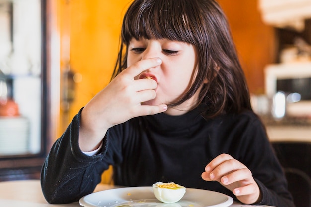 Hübsches Mädchen, das Hälfte des Eies in der Küche isst