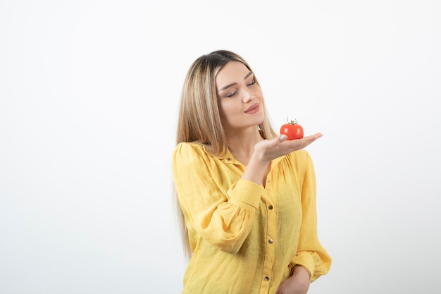 hübsches Mädchen, das rote Tomate auf Weiß betrachtet.