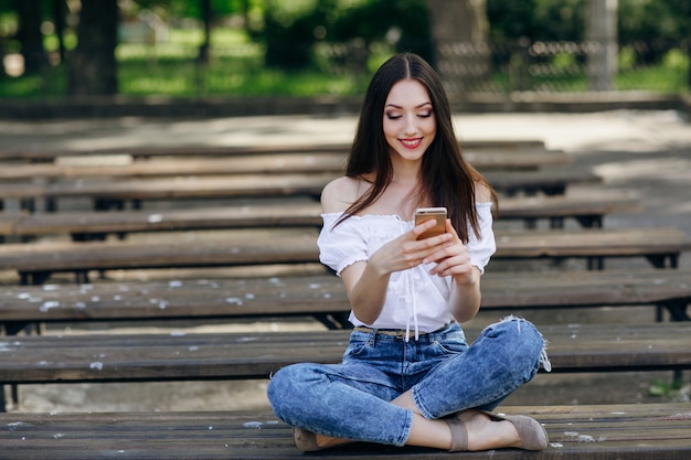 Hübsches Mädchen, das Schreiben auf ihr Handy auf der Bank sitzt in einem Park