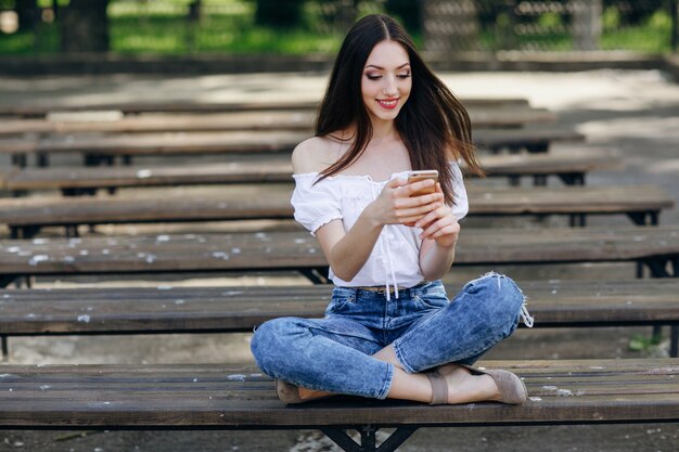 Hübsches Mädchen, das Schreiben auf ihr Handy auf der Bank sitzt in einem Park