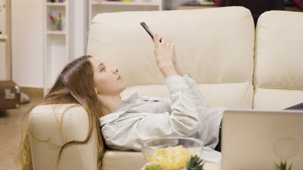 Hübsches Mädchen, das sich mit ihrem Smartphone auf der Couch entspannt. Freund im Hintergrund.