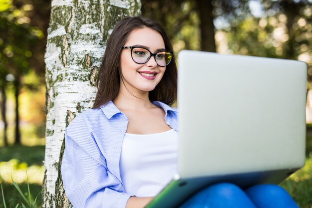 Hübsches Mädchen in Blue Jeans arbeiten mit Laptop im sonnigen Tag des Stadtparks