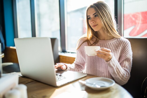 Hübsches Mädchen in einem modischen Pullover, sitzend in einem Café mit einer Tasse Tee Kaffee, der in die Kamera schaut