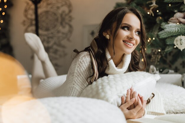 Hübsches Mädchen liegt mit Kissen nahe einem Weihnachtsbaum