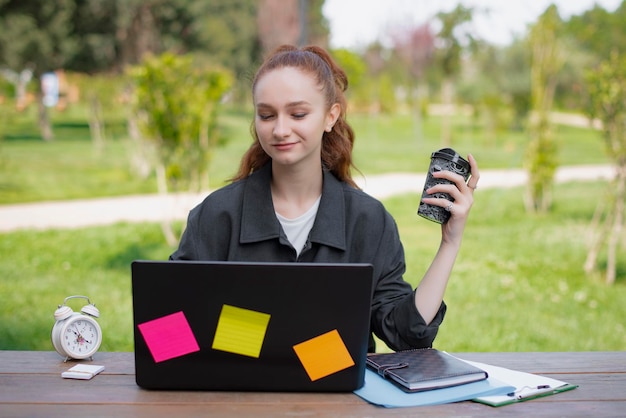 Hübsches Mädchen mit roten Haaren, das am Laptop-Kaffeebetrieb arbeitet