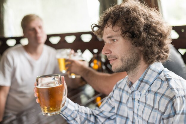 Hübsches männliches trinkendes Bier nahe Freunden in der Stange