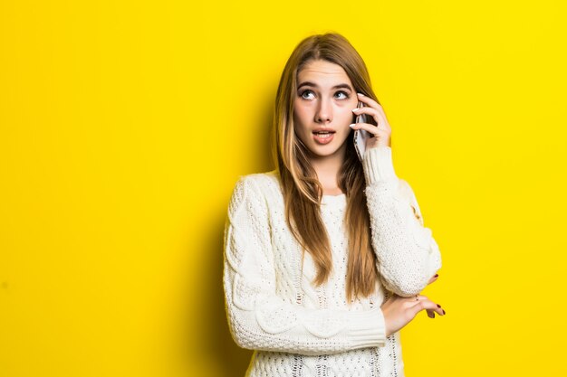 Hübsches modisches Mädchen hat einen Telefonanruf, der breiten weißen Pullover auf Gelb trägt