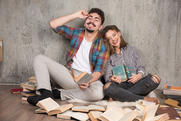 hübsches Paar, das mit vielen Büchern auf dem Boden sitzt