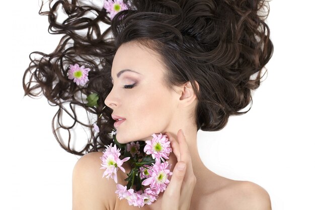 Hübsches schönes Mädchen, das mit hellen Blumen in ihrem hellen Haarschminke lokalisiert auf Weiß liegt
