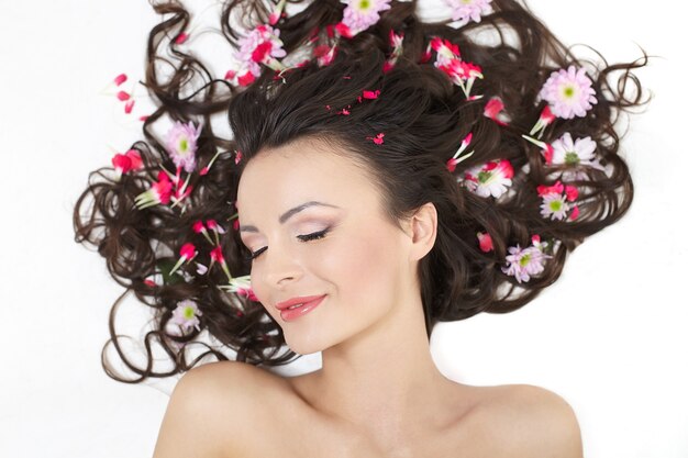 Hübsches schönes Mädchen, das mit leuchtend roten Blumen in ihrem hellen Haarschminke lokalisiert auf Weiß liegt