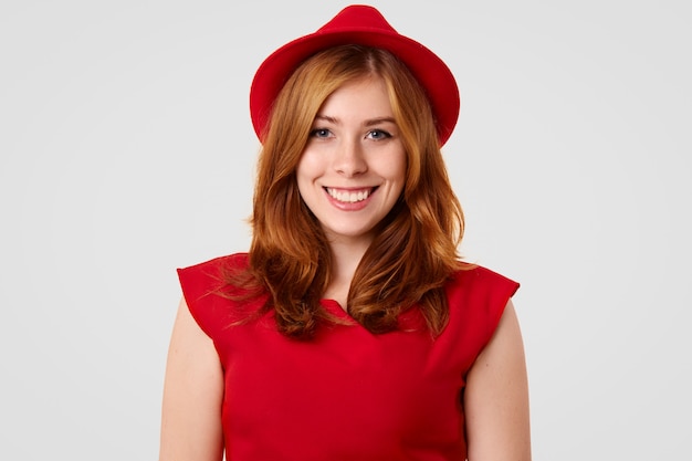 Hübsches weibliches Model mit positivem Lächeln, gekleidet in eleganten roten Hut und Bluse, Verabredung mit Freund