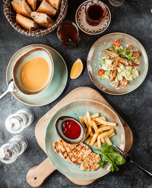 Hühnchensteak mit Pommes Frites und Ketchup, serviert mit Suppe und Caesar-Salat