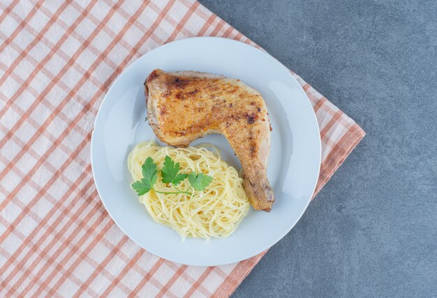 Hühnerbein und Spaghetti auf weißem Teller.