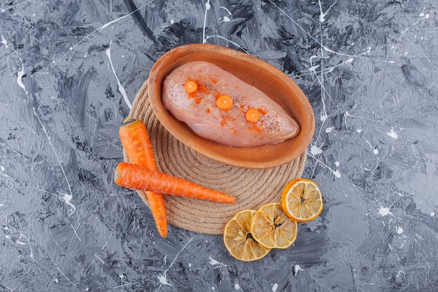 Hühnerbrust in einer Schüssel neben Karotten und Zitrone auf einem Untersetzer auf der blauen Oberfläche