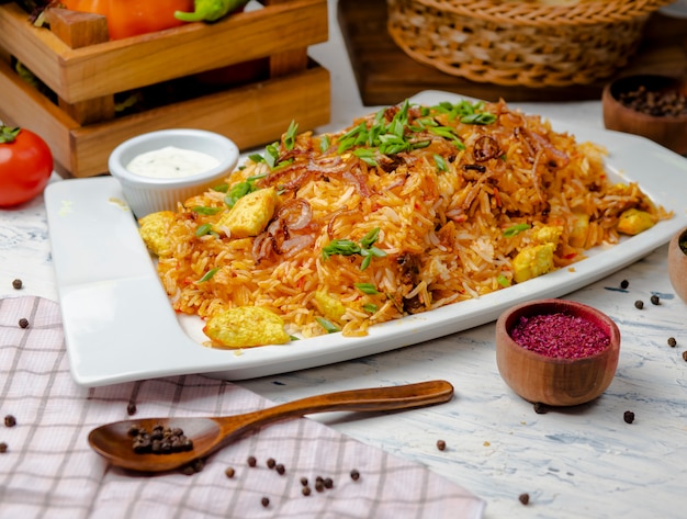 Hühnerbrust, Tomatensauce, Reis, Risotto, Plov mit Kräutern, Joghurt und Sumakh in der weißen Platte