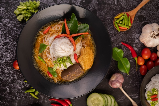 Hühnercurry in einer schwarzen Tasse mit Reisnudeln.