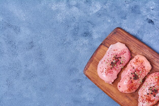 Hühnerfilet mit Gewürzen auf einem Holzbrett auf blau