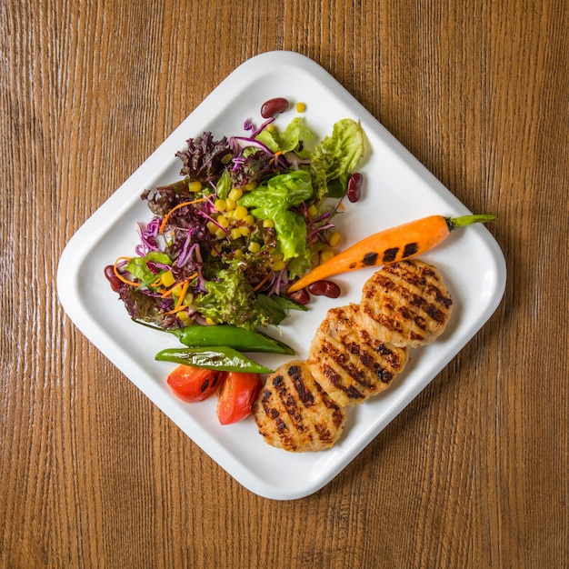 Hühnerfiletcotlets der Draufsicht mit grünem Salat und Karotte.