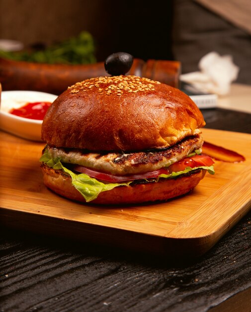 Hühnerfleischburger mit Tomatenscheiben und Kopfsalat diente mit, Ketschup und Majonäse auf hölzernem Brett