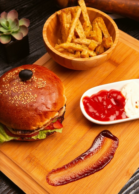 Hühnerfleischburger mit Tomatenscheiben und Kopfsalat diente mit Pommes-Frites, Ketschup und Majonäse auf hölzernem Brett