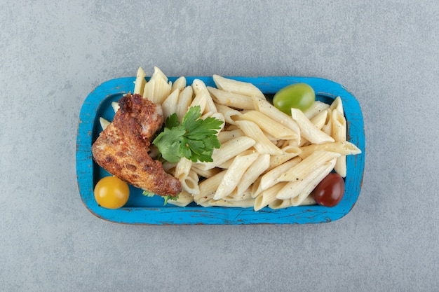 Hühnerflügel mit Penne-Nudeln auf blauem Teller.