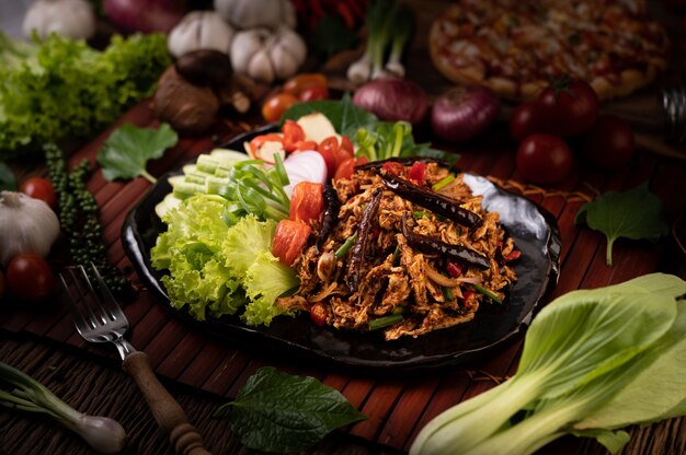 Hühnerlarb auf dem Teller Mit getrockneten Chilis, Tomaten, Frühlingszwiebeln und Salat