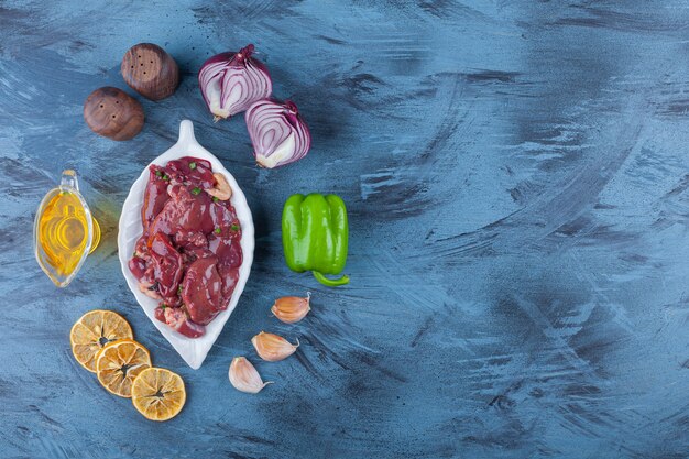 Hühnernebenerzeugnisse auf einer Platte, Ölschale, Salz, Zwiebel, Knoblauch und Pfeffer, auf dem blauen Hintergrund.