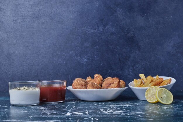 Hühnernuggets mit Kartoffeln und Saucen in weißen Tellern.