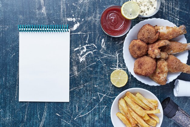 Hühnernuggets mit Kartoffeln und Saucen mit einem Notizbuch beiseite.