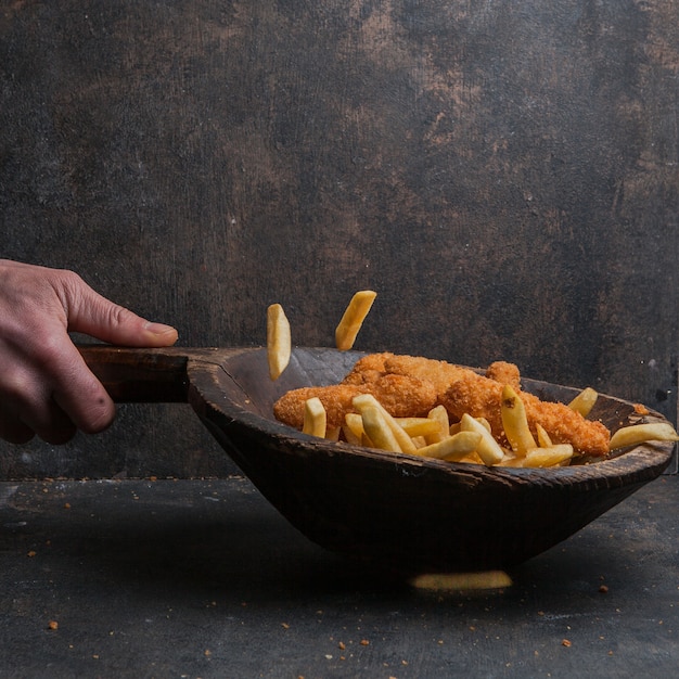 Kostenloses Foto hühnernuggets mit pommes frites und menschlicher hand in holzteller