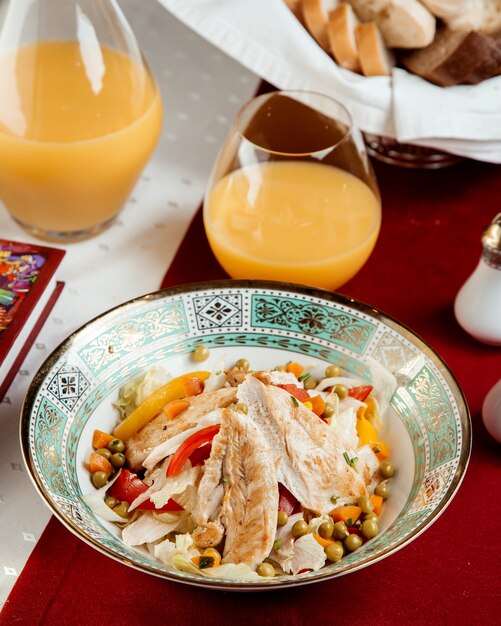 Hühnersalat mit Paprikaerbsen und einem Glas Orangensaft