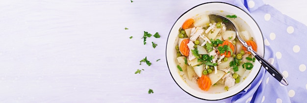 Hühnersuppe mit grünen Erbsen, Karotten und Kartoffeln in einer weißen Schüssel