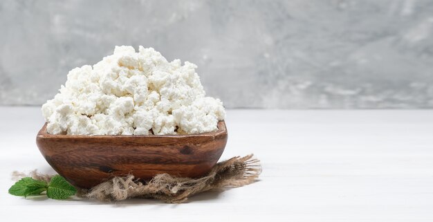 Hüttenkäse in einer traditionellen Holzschale auf weißem Hintergrund aus Holz. Nahaufnahme, selektiver Fokus mit Kopienraum. Weicher Quark natürliches gesundes Essen, vollwertige Diätnahrung