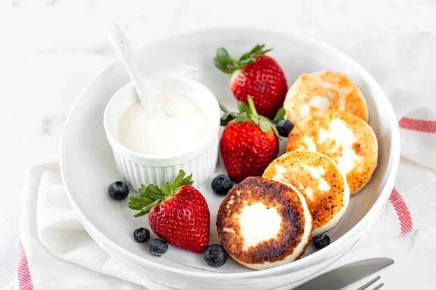 Kostenloses Foto hüttenkäse-pancakes käsekuchen ricotta-fritter mit frischen erdbeeren und blaubeeren aus einem weißen keramikteller gesundes und leckeres frühstück für den feiertag