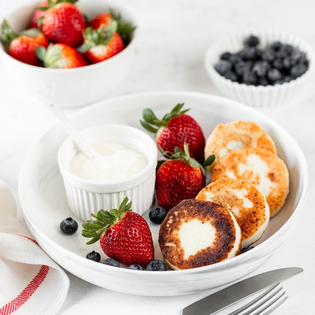 Hüttenkäse-Pancakes Käsekuchen Ricotta-Fritter mit frischen Erdbeeren und Blaubeeren aus einem weißen Keramikteller Gesundes und leckeres Frühstück für den Feiertag