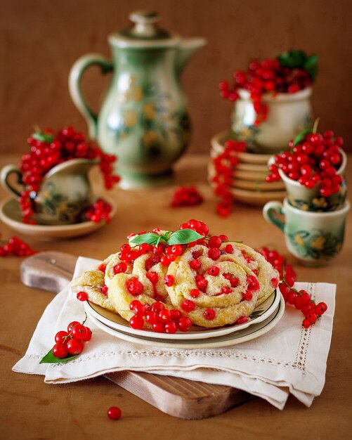 Hüttenkäseplätzchen rollt mit roten Johannisbeeren auf keramischer Platte mit keramischem Tee- oder Kaffeesatz der Weinlese, Teezeit, Frühstück, Sommerbonbons