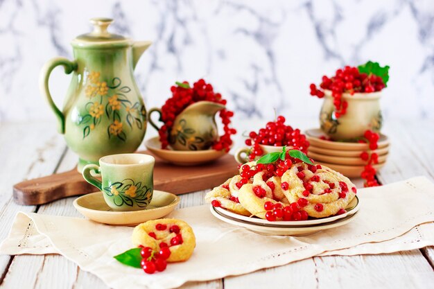 Hüttenkäseplätzchen rollt mit roten Johannisbeeren auf keramischer Platte mit keramischem Tee- oder Kaffeesatz der Weinlese, Teezeit, Frühstück, Sommerbonbons