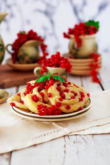 Hüttenkäseplätzchen rollt mit roten Johannisbeeren auf keramischer Platte mit keramischem Tee- oder Kaffeesatz der Weinlese, Teezeit, Frühstück, Sommerbonbons