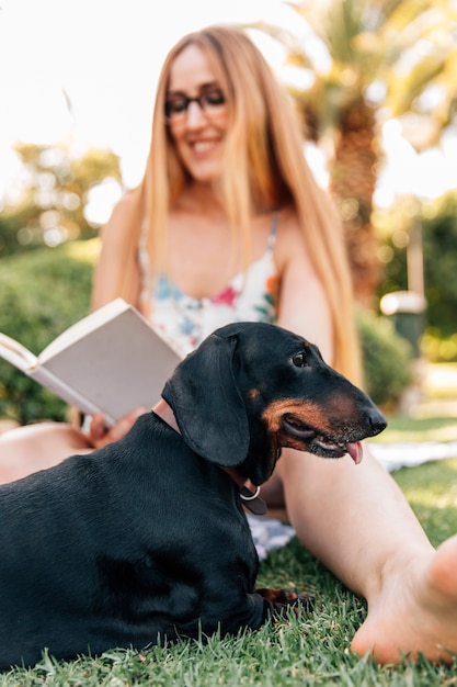 Hund, der vor lächelndem Buch der jungen Frau Lese sitzt