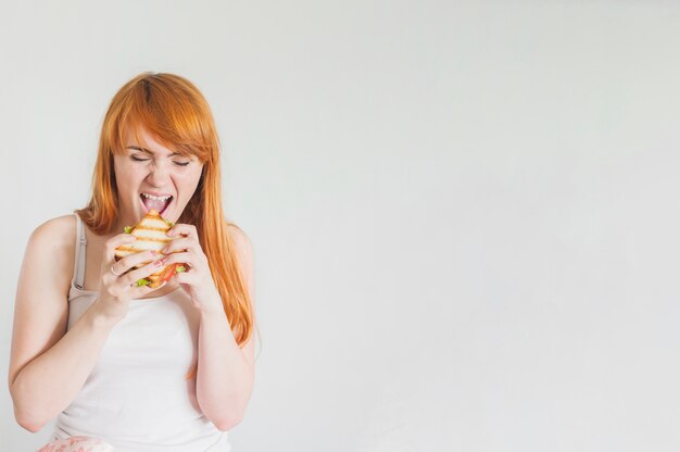 Hungrige junge Frau, die gegrilltes Sandwich gegen weißen Hintergrund isst