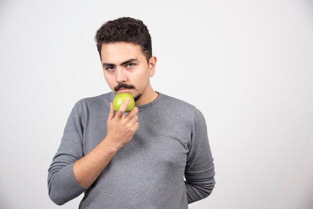 Hungriger Mann, der grünen Apfel hält und ernst schaut.