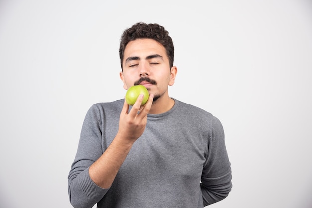 Hungriger Mann riecht grünen Apfel auf grau.