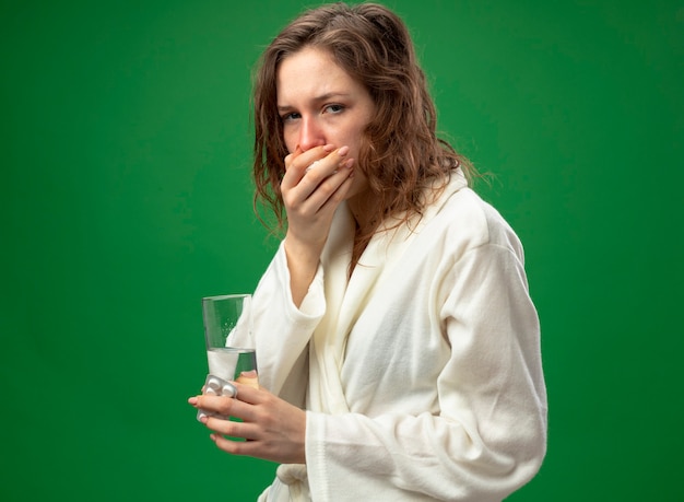 Kostenloses Foto husten junges krankes mädchen, das weißes gewand trägt, das glas wasser hält und hand auf mund lokalisiert auf grün setzt