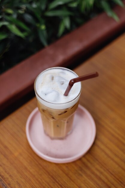 Iced Latte in Glas auf einem rosa Ständer auf Holztisch in Sommercafégrünbüschen